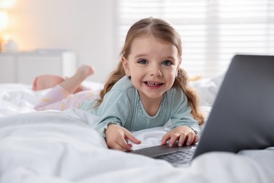 Cute little girl using laptop on bed at home