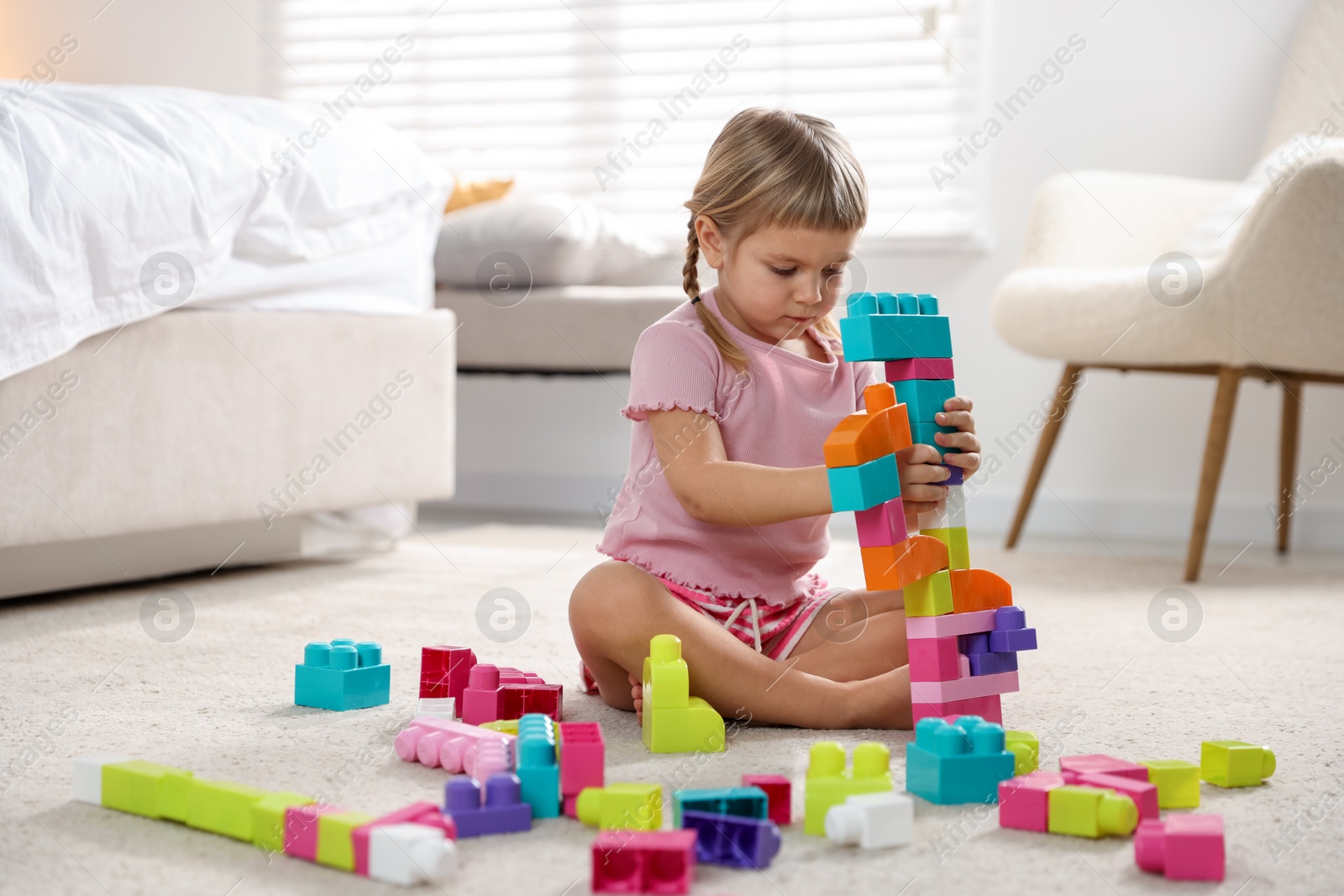 Photo of Cute little girl playing with colorful building blocks on floor at home