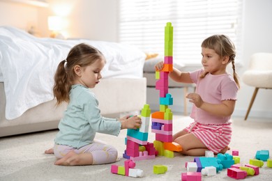 Photo of Cute little sisters playing with colorful building blocks on floor at home