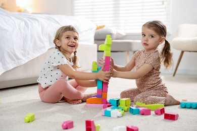 Photo of Cute little sisters playing with colorful building blocks on floor at home