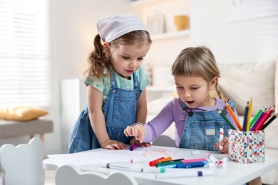 Cute little sisters drawing at white table in room