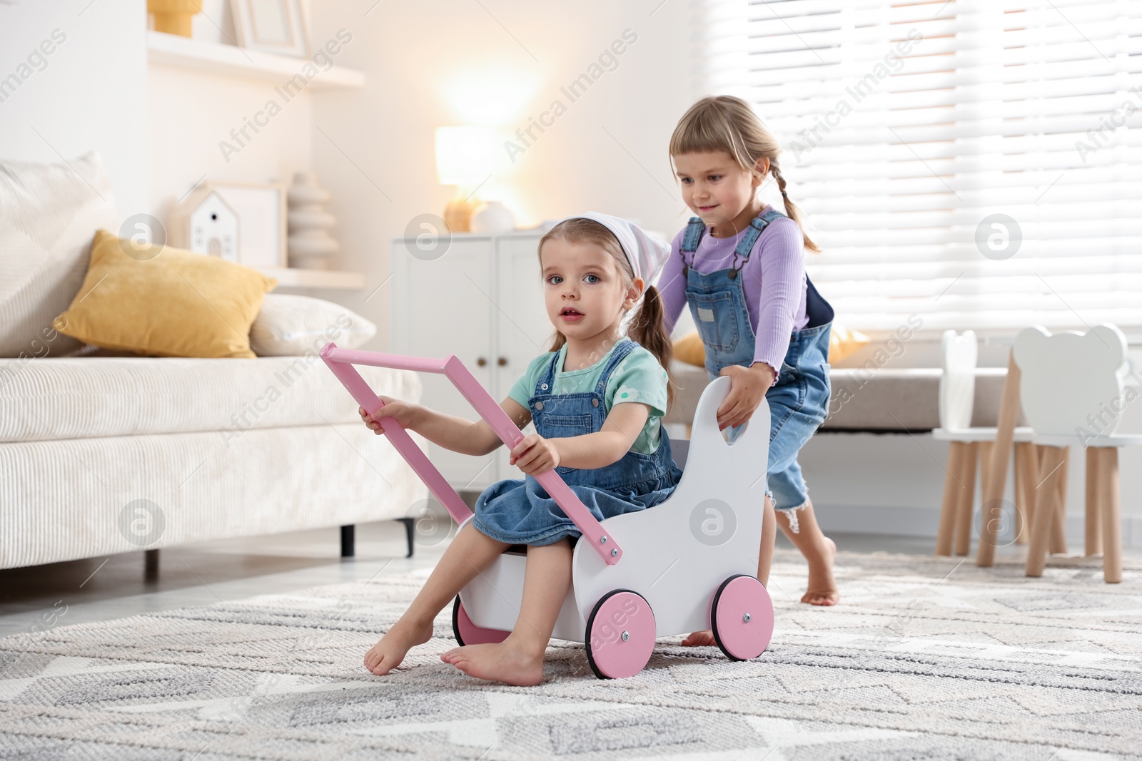 Photo of Cute little sisters playing with toy stroller at home