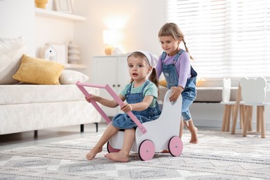 Cute little sisters playing with toy stroller at home