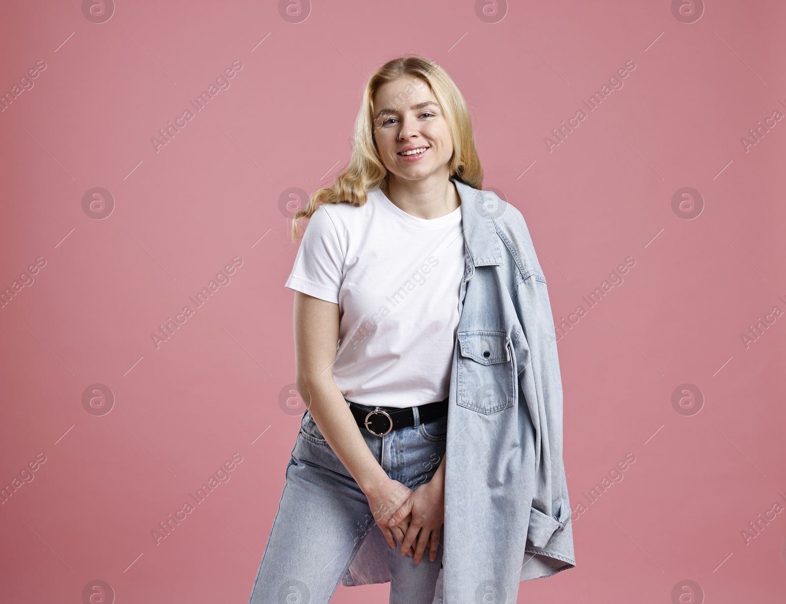 Photo of Smiling woman in stylish jeans on pink background