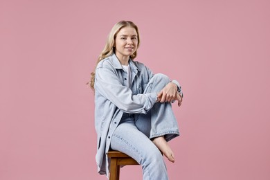 Photo of Smiling woman in stylish jeans sitting on stool against pink background