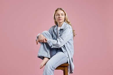 Photo of Beautiful young woman in stylish jeans sitting on stool against pink background