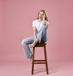 Photo of Smiling woman in stylish jeans sitting on stool against pink background