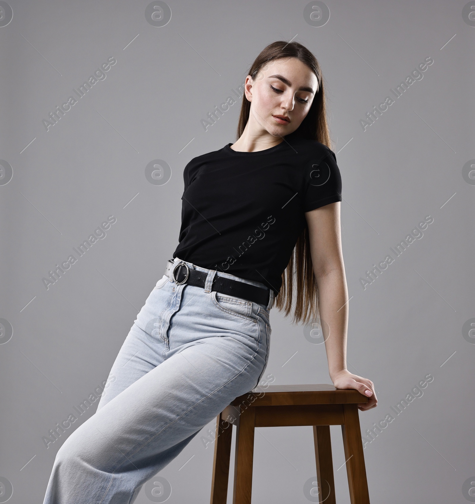 Photo of Woman in stylish jeans and stool against grey background, low angle view