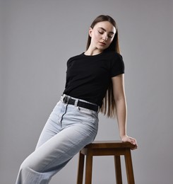 Woman in stylish jeans and stool against grey background, low angle view