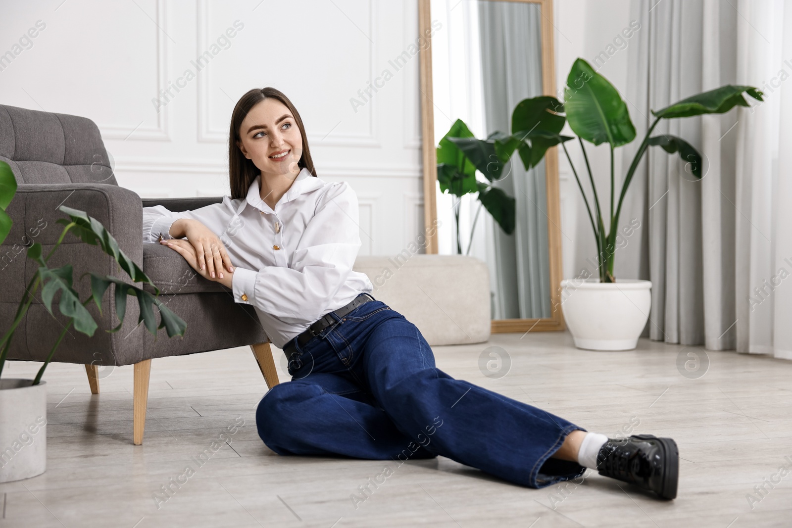 Photo of Smiling woman in stylish jeans sitting on floor at home