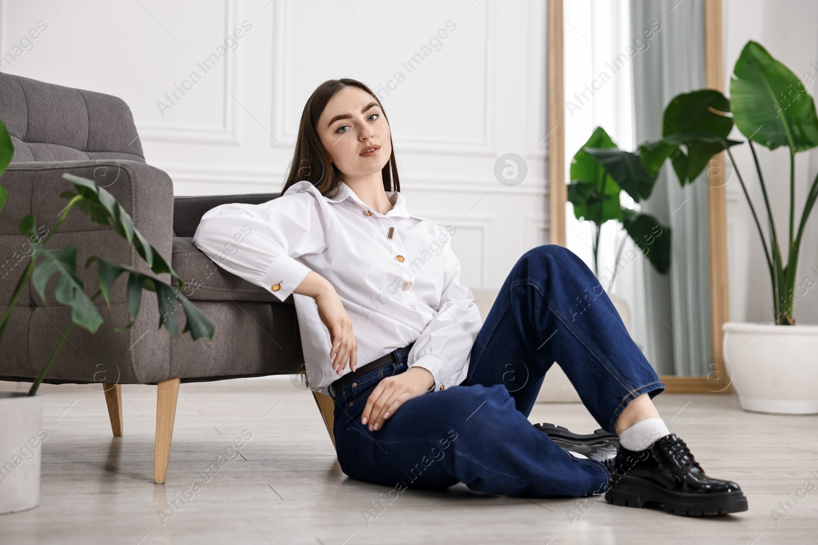 Photo of Beautiful young woman in stylish jeans sitting on floor at home