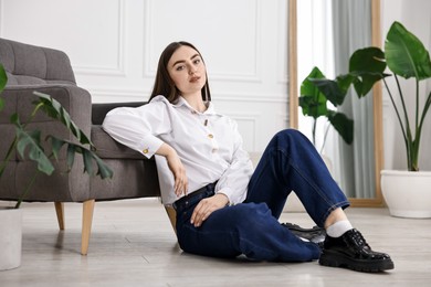 Photo of Beautiful young woman in stylish jeans sitting on floor at home