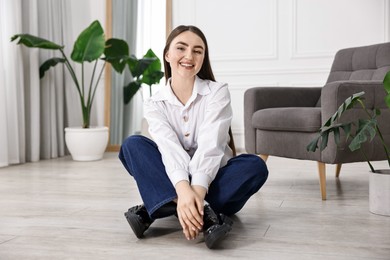 Smiling woman in stylish jeans sitting on floor at home