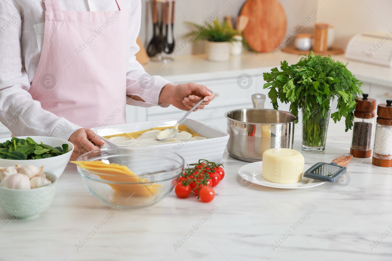 Photo of Woman spreading bechamel sauce onto spinach lasagna at marble table indoors, closeup