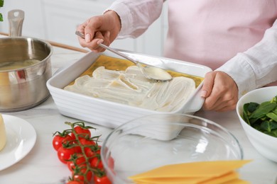 Woman spreading bechamel sauce onto spinach lasagna at marble table indoors, closeup