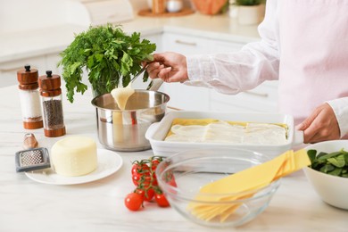 Woman spreading bechamel sauce onto spinach lasagna at marble table indoors, closeup