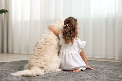 Little girl with cute dog on carpet at home, back view