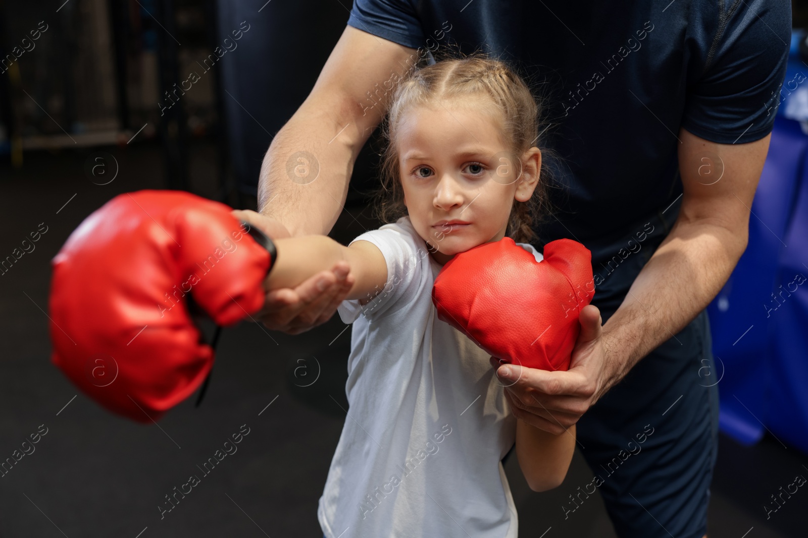 Photo of Girl in protective gloves having boxing practice with her coach at training center