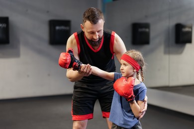 Photo of Girl in protective gloves having boxing practice with her coach at training center