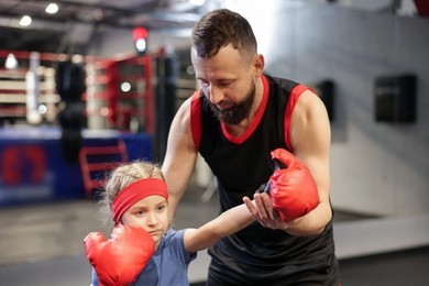 Photo of Girl in protective gloves having boxing practice with her coach at training center