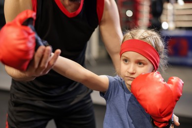 Girl in protective gloves having boxing practice with her coach at training center