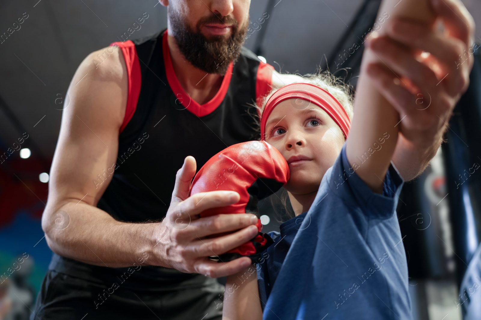 Photo of Girl in protective gloves having boxing practice with her coach at training center