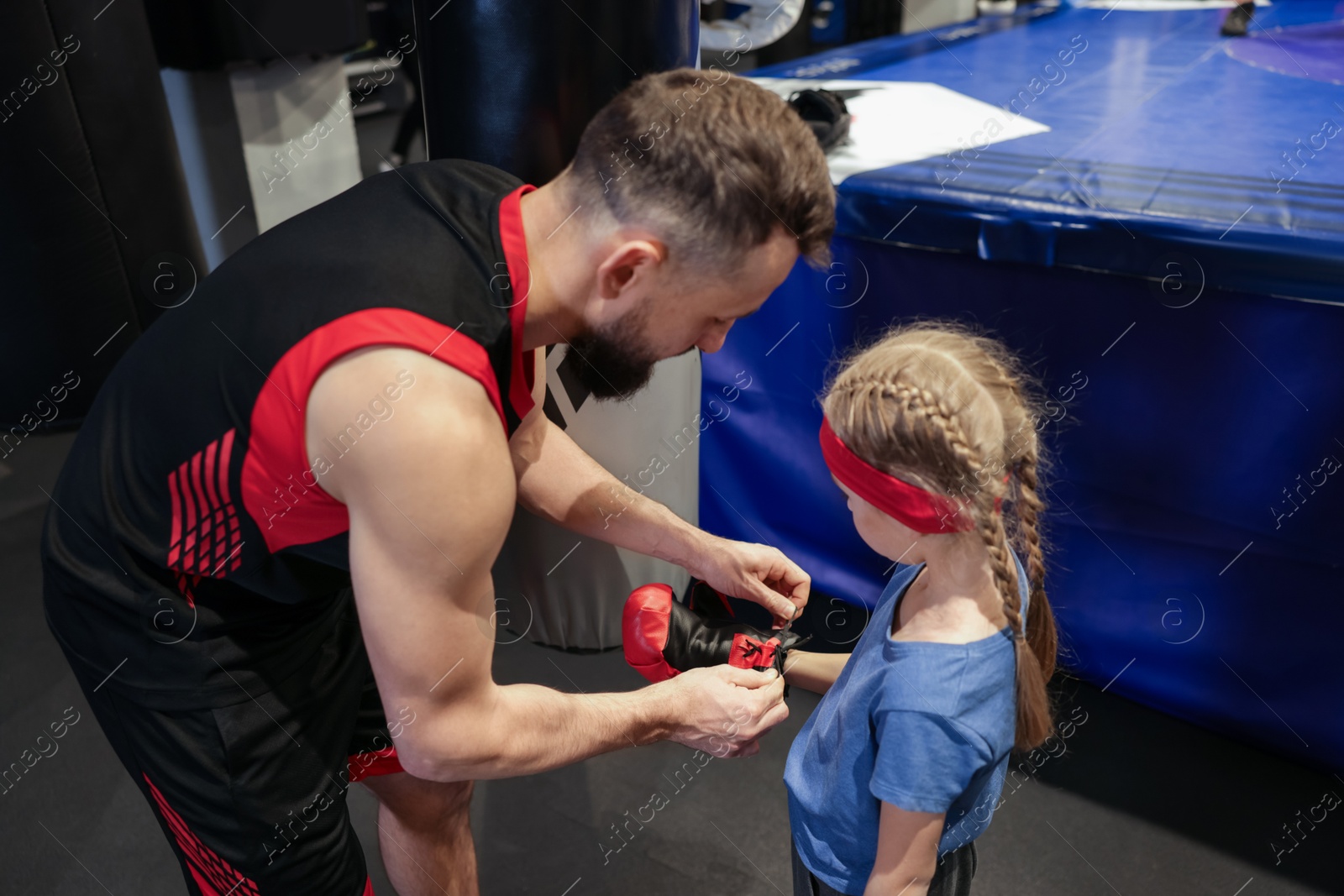 Photo of Boxing. Coach helping girl to put on protective gloves before training indoors