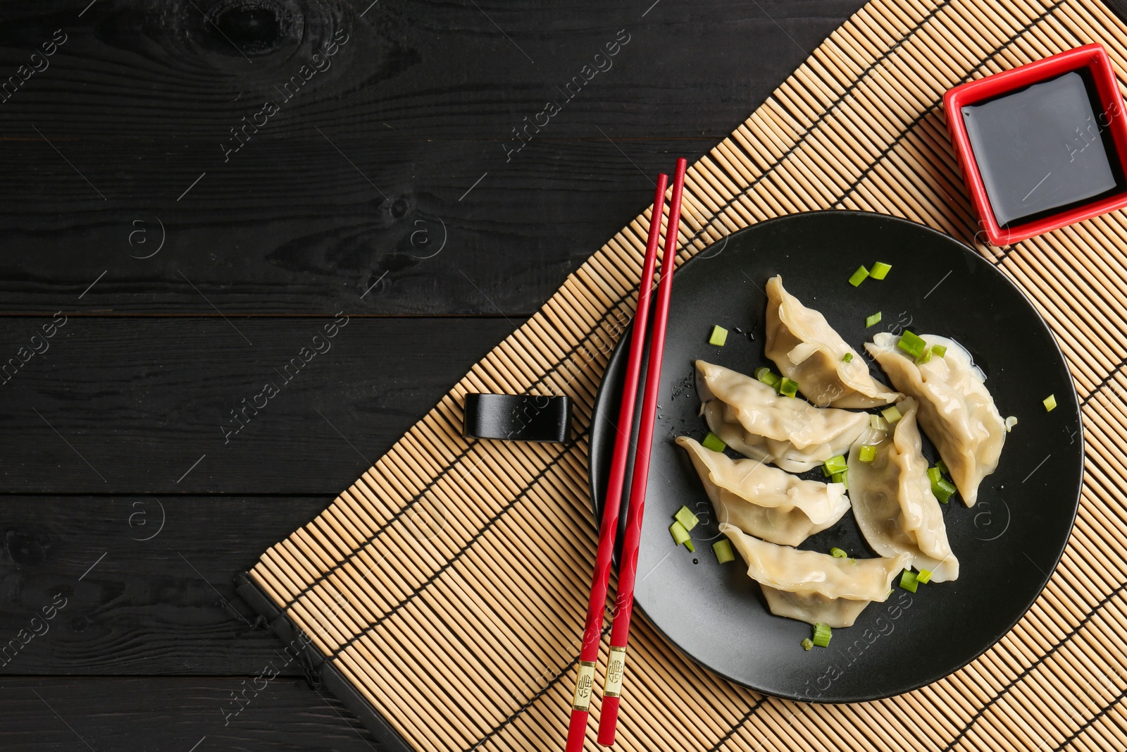 Photo of Delicious gyoza dumplings with chives served on black wooden table, top view. Space for text