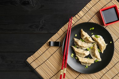 Photo of Delicious gyoza dumplings with chives served on black wooden table, top view. Space for text