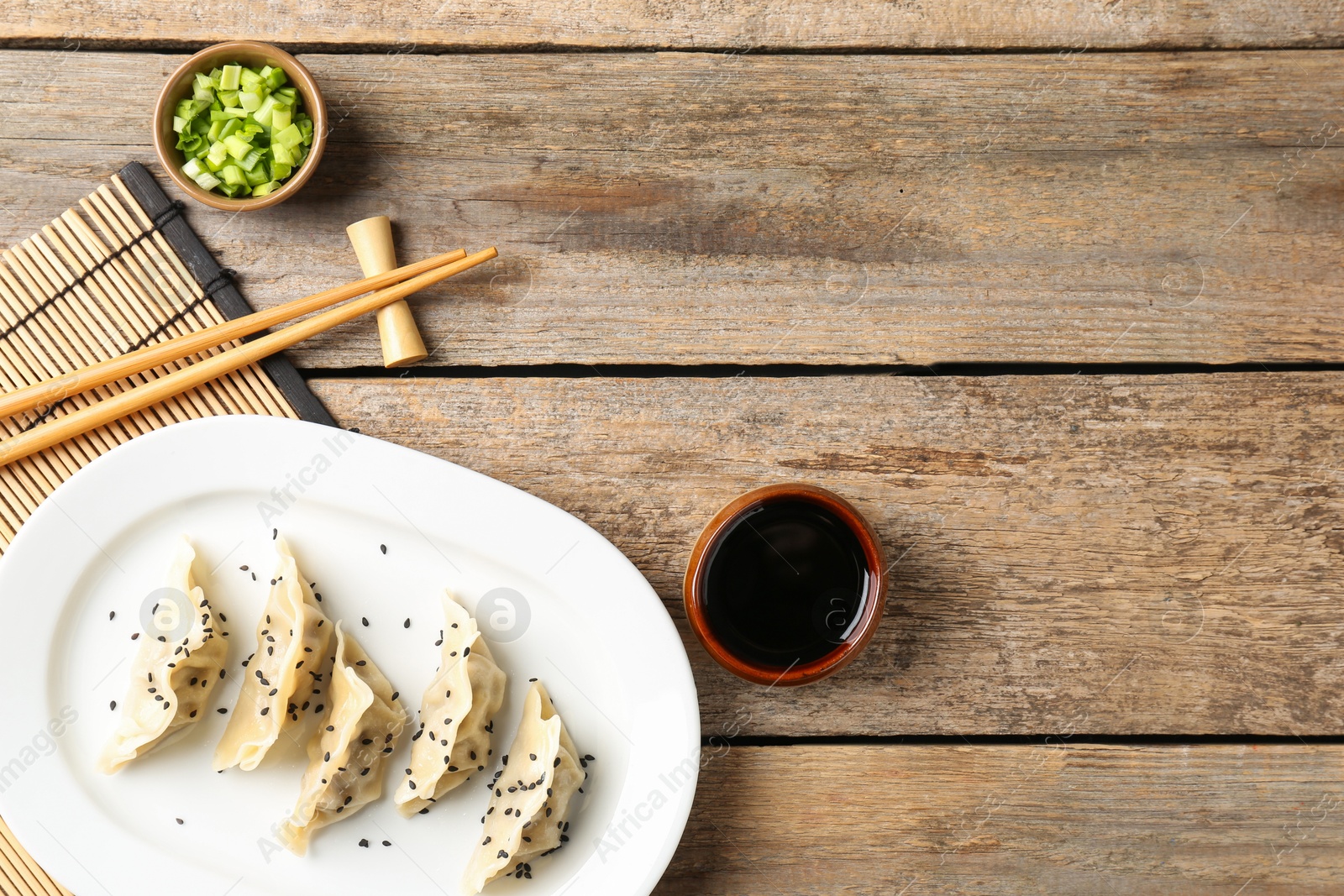 Photo of Delicious gyoza dumplings with sesame seeds served on wooden table, top view. Space for text