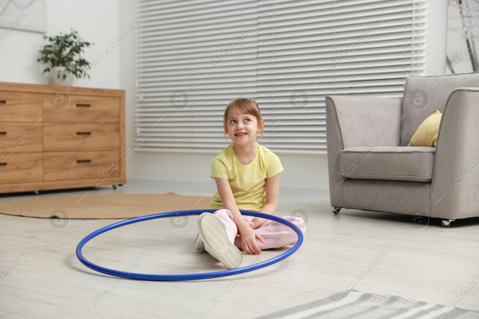 Photo of Cute little girl with hula hoop on floor at home