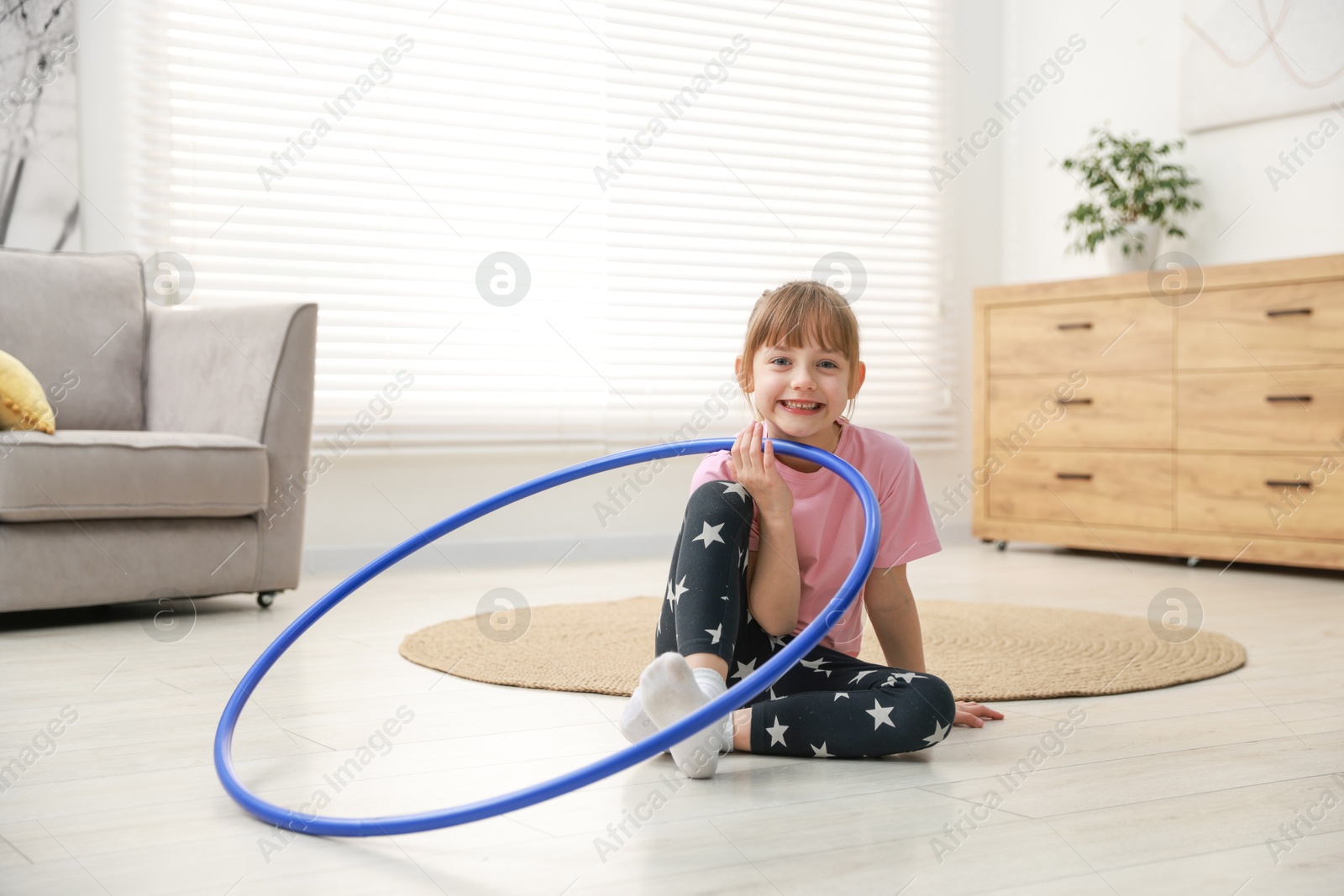 Photo of Cute little girl with hula hoop on floor at home