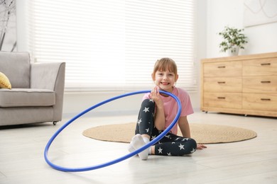 Photo of Cute little girl with hula hoop on floor at home