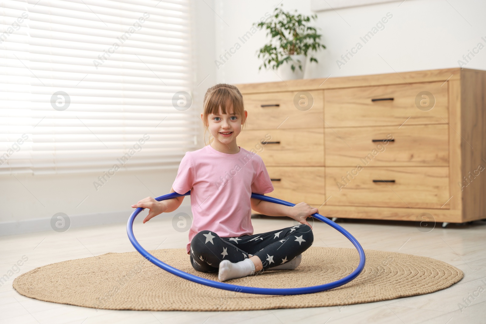 Photo of Cute little girl with hula hoop on floor at home