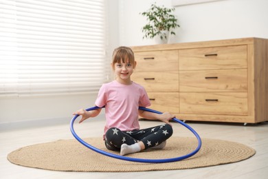 Photo of Cute little girl with hula hoop on floor at home