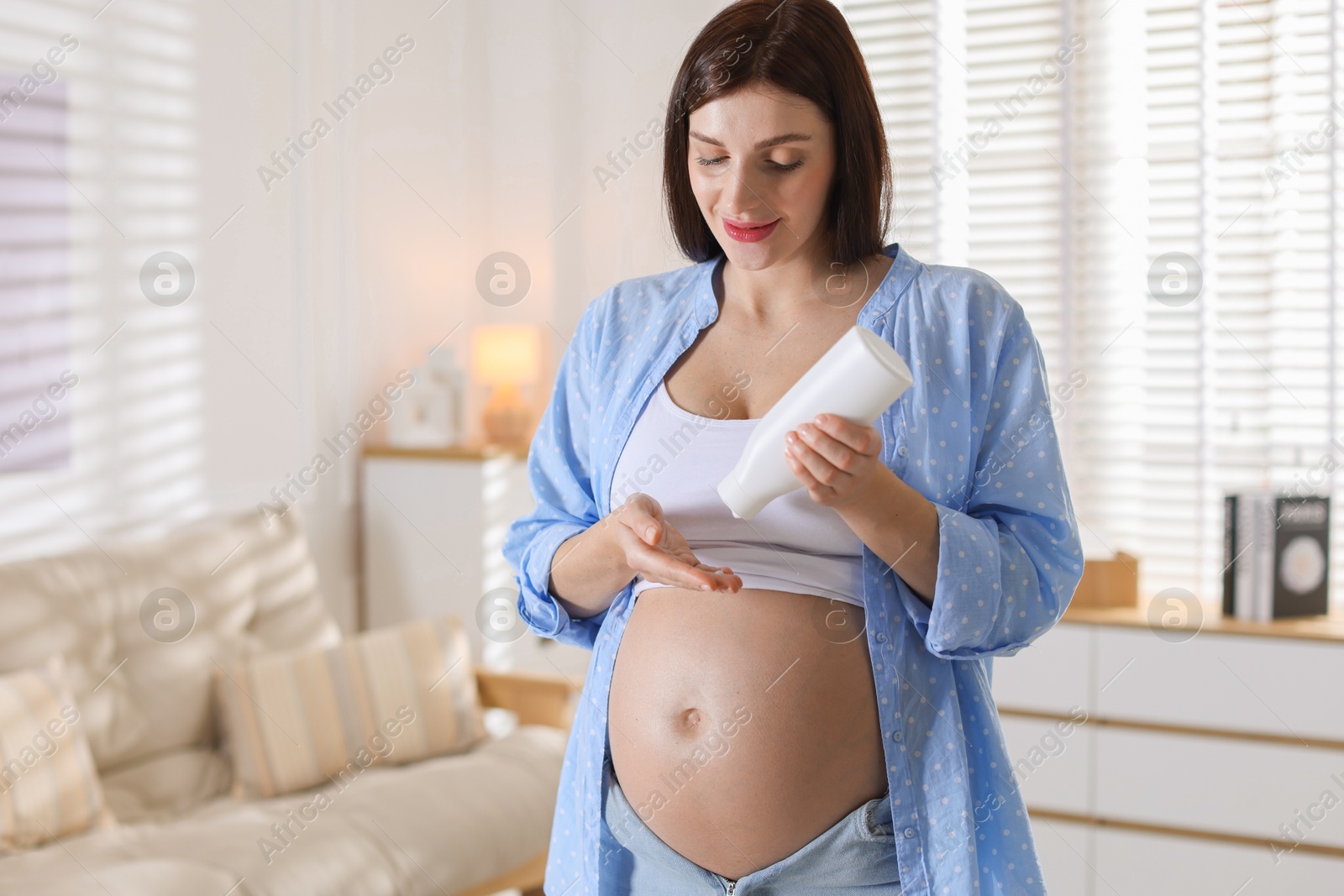 Photo of Beautiful pregnant woman applying cream on belly at home