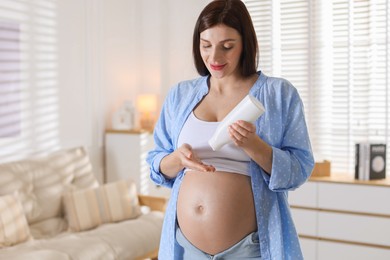 Beautiful pregnant woman applying cream on belly at home