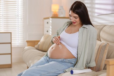 Beautiful pregnant woman applying cream on belly at home