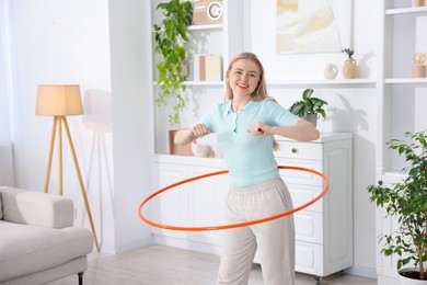 Photo of Beautiful young woman exercising with hula hoop at home