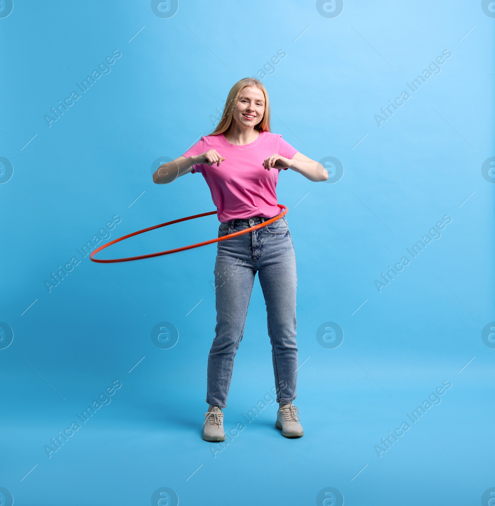 Photo of Beautiful young woman exercising with hula hoop on light blue background