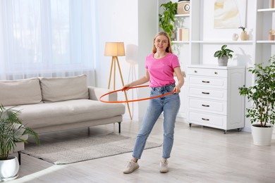 Photo of Beautiful young woman exercising with hula hoop at home