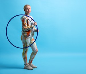 Photo of Beautiful young woman with hula hoop on light blue background, space for text