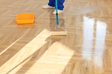 Photo of Man polishing parquet with varnish indoors, closeup