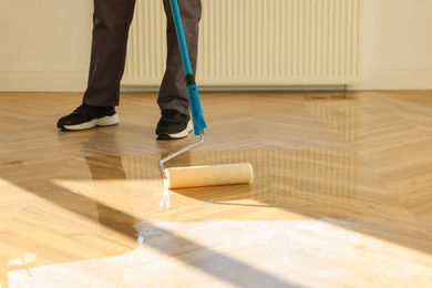 Man polishing parquet with varnish indoors, closeup. Space for text