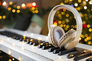 Photo of Headphones on electric piano against Christmas tree with blurred lights, closeup. Bokeh effect