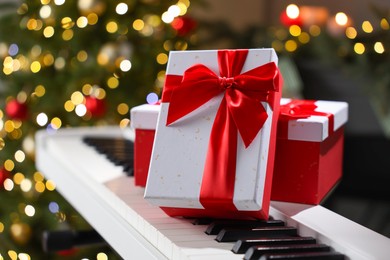 Photo of Gifts on electric piano against Christmas tree with blurred lights, closeup. Bokeh effect