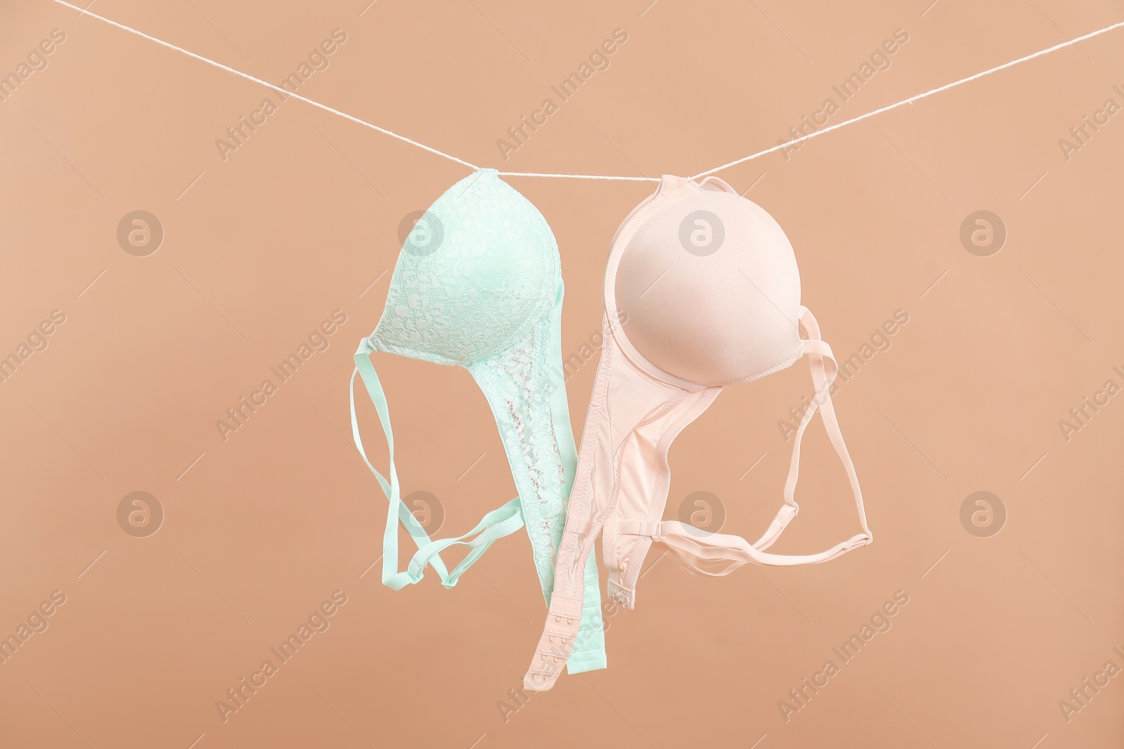 Photo of Beautiful bras hanging on rope against dark beige background