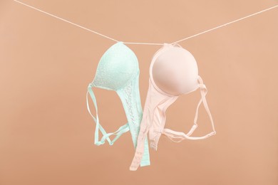 Photo of Beautiful bras hanging on rope against dark beige background