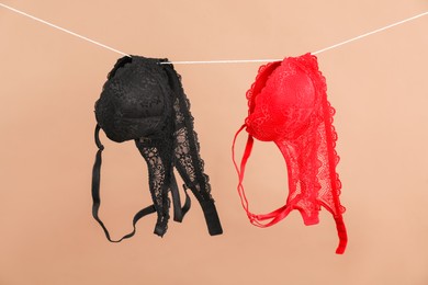 Photo of Beautiful bras hanging on rope against dark beige background