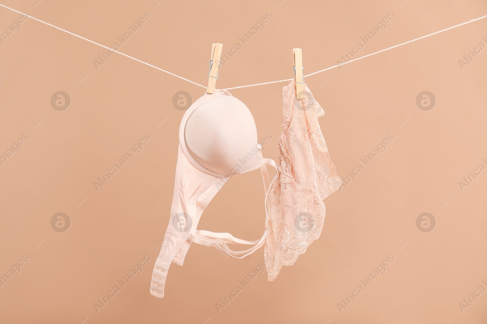 Photo of Beautiful bra and panties hanging on rope against dark beige background